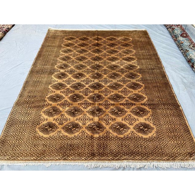 This warm Turkmen Bokhara rug features a dense grid of small octagonal medallions, each finely detailed with a stylized...