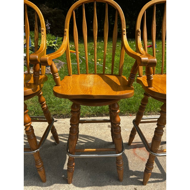 A matching set of four solid oak Windsor-style swivel bar stools produced by the Virginia House Furniture Corporation...