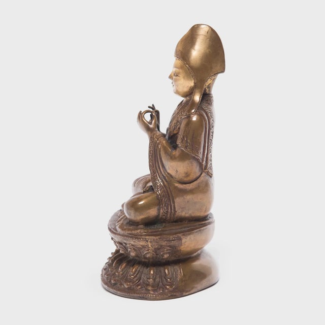 Cast in brass with a rich patina, this seated figure is a Lama, a spiritual master and teacher of the Dharma in Tibetan...