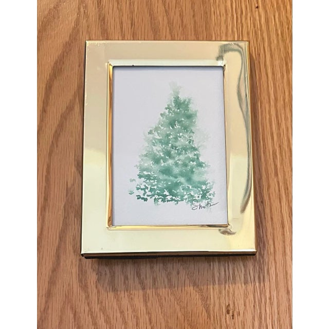 A serene and minimal watercolor painting of a soft, snow-dusted evergreen tree, capturing the quiet beauty of winter. The...