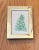 A serene and minimal watercolor painting of a soft, snow-dusted evergreen tree, capturing the quiet beauty of winter. The...