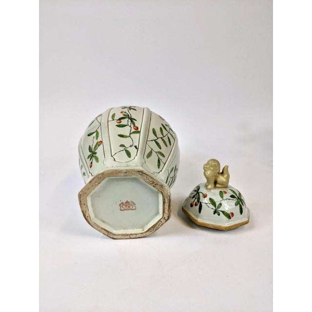 This is a late 20th Century temple jar hand painted with flower buds and butterflies. A small foo dog perches on the top...