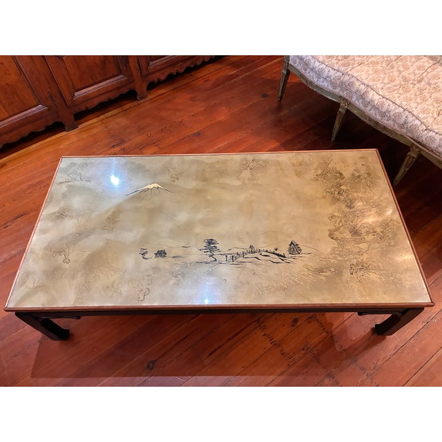 A large, Asian style mid 20th century coffee table, with a mountain landscape simply rendered on a sage, gray- green top....