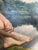 A striking early to mid-20th century oil on board by J.M. Robinson, depicting a seated nude figure beside a quiet body of...