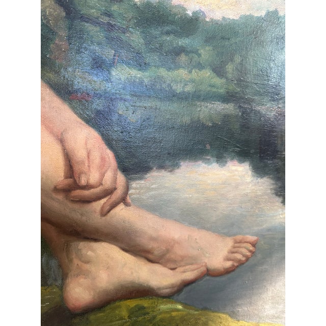 A striking early to mid-20th century oil on board by J.M. Robinson, depicting a seated nude figure beside a quiet body of...