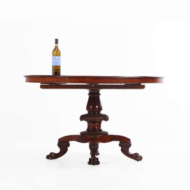 A fine 19th-century mahogany pedestal dining table, featuring a shaped and intricately carved central pedestal shaft...