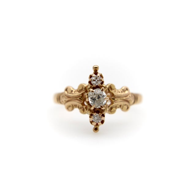This 14k gold Victorian ring contains three diamonds in a north-south arrangement. The larger, central diamond is an Old...