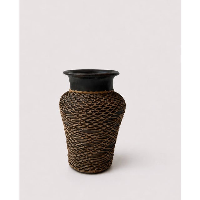 This ceramic vase is wrapped in a handwoven rattan sleeve that partly conceals the lower body while leaving the glazed...