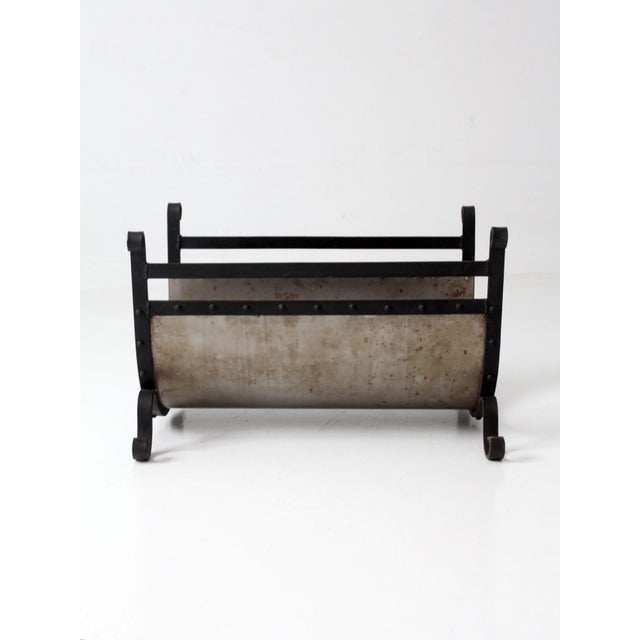 A vintage mid-century fireplace log holder combining a curved steel cradle with a dark iron frame, riveted construction,...