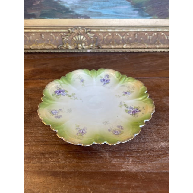 Decorative cabinet plate featuring a scalloped, molded edge and hand-painted floral decoration. The plate is designed with...