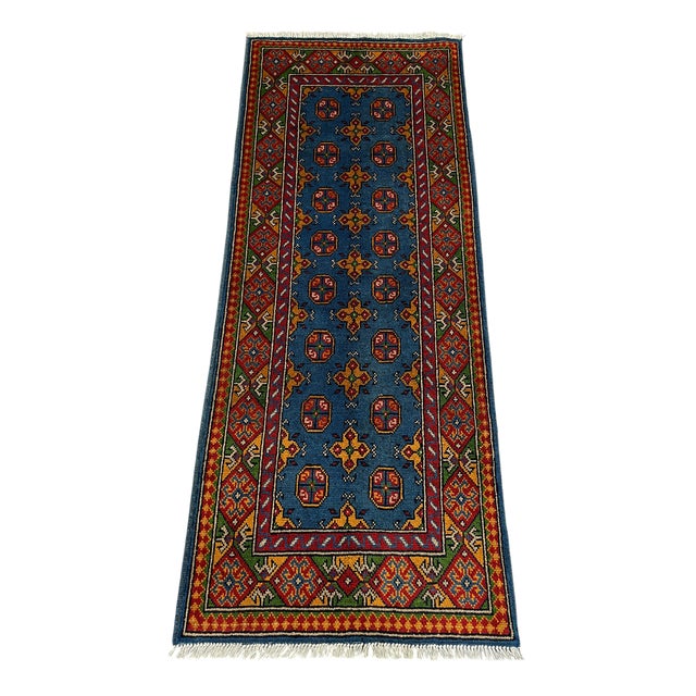 This tribal Oriental wool runner has a rich blue field patterned with two rows of small octagonal medallions and golden...