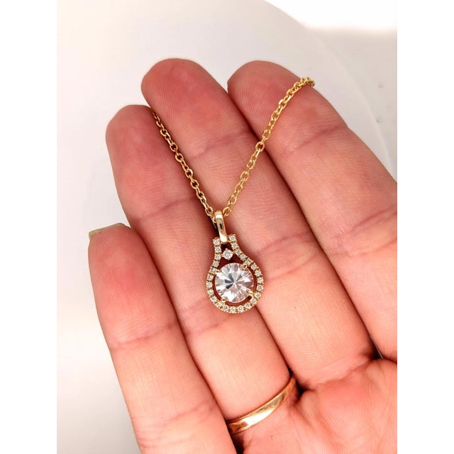 A white zircon glows with white brilliance at the heart of this round pendant, framed by a trail of brilliant natural...