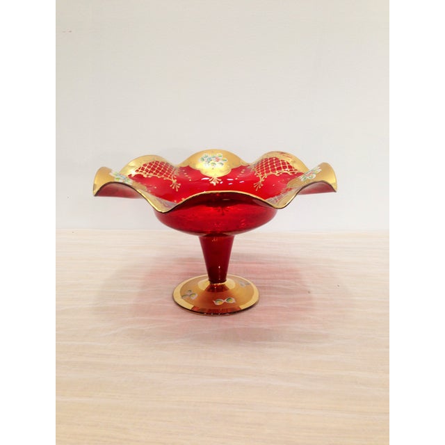 Red glass compote with ornate, hand-painted gold detailing. Tiny, color floral motifs on edges.