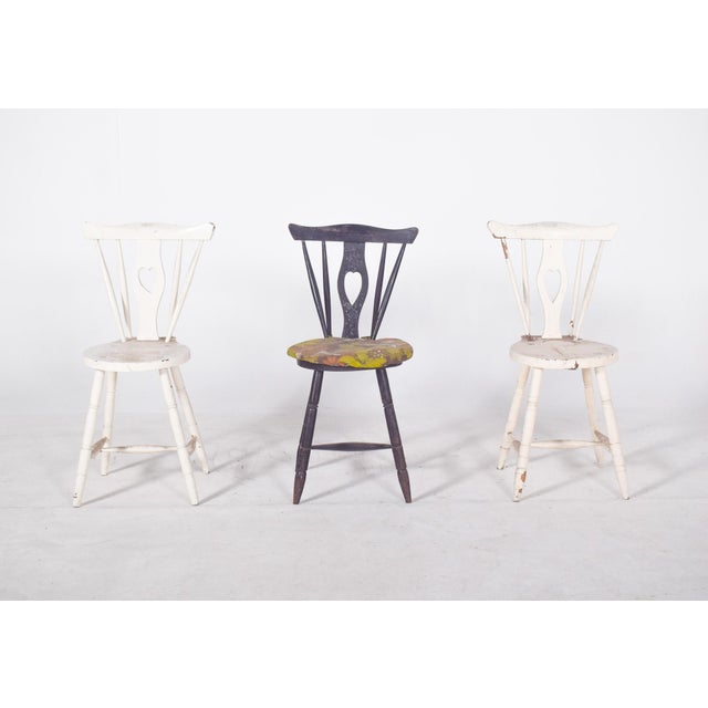 Three chairs with codtail backs. Painted wood, with cut-out backs and a hollowed-out ‘heart’ silhouette, evoking a...