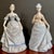 A graceful pair of vintage porcelain figurines depicting Victorian ladies in flowing blue gowns, each rendered with...