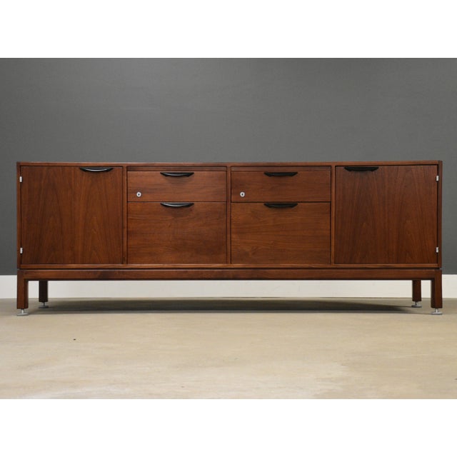A mid century modern walnut long sideboard credenza designed by Jens Risom with sculpted black drawer pulls and cabinet...
