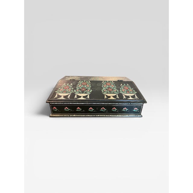 A charming vintage slant-front correspondence box featuring a black lacquered finish adorned with hand-painted floral...