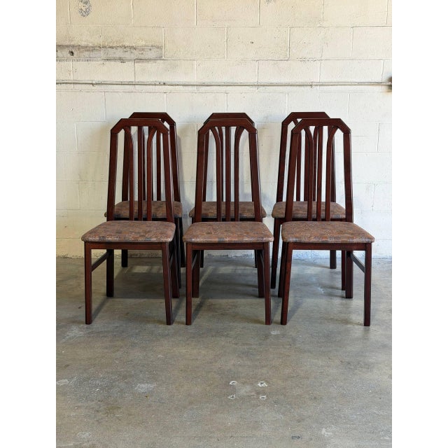 This set of 6 dining chairs features tall slatted backrests with geometric arched frames. Crafted with dark stained wood...