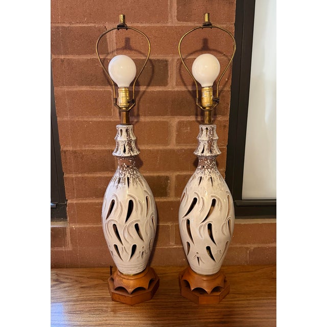 A striking pair of vintage Mid-Century Modern ceramic table lamps featuring an intricately pierced cutout design and...