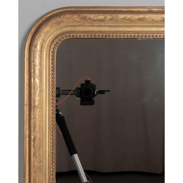 An early 20th century French Louis Philippe style gilded mirror with curved top corners, incised floral decoration and...