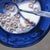 This artwork depicts a close-up view of a bowl filled with cereal, surrounded by the contrasting blue of the bowl and the...
