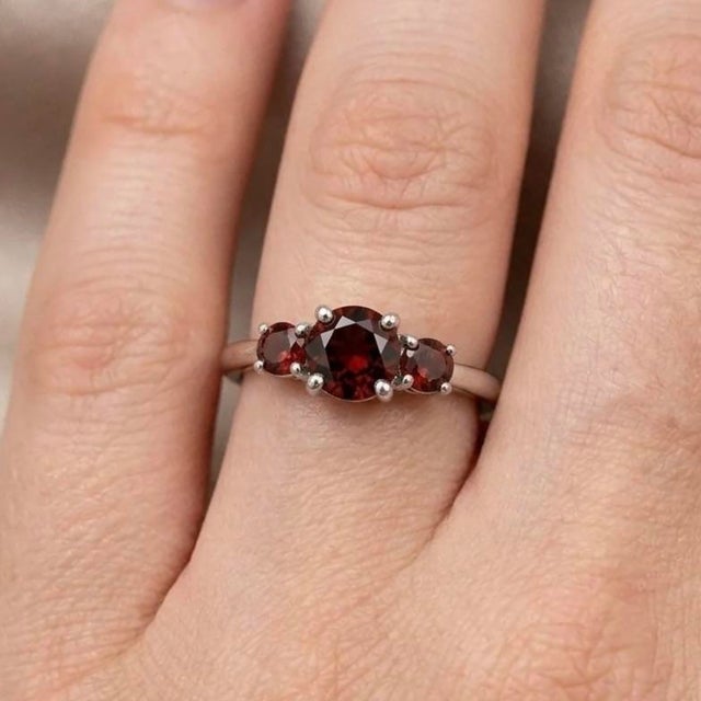 This elegant ring features a timeless trio of Garnet gemstones, admired for their deep red hue and rich, captivating...