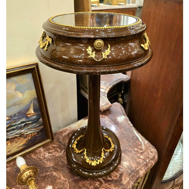 This elegant French style side table features a rich dark wood finish accented with refined gold leaf details that...