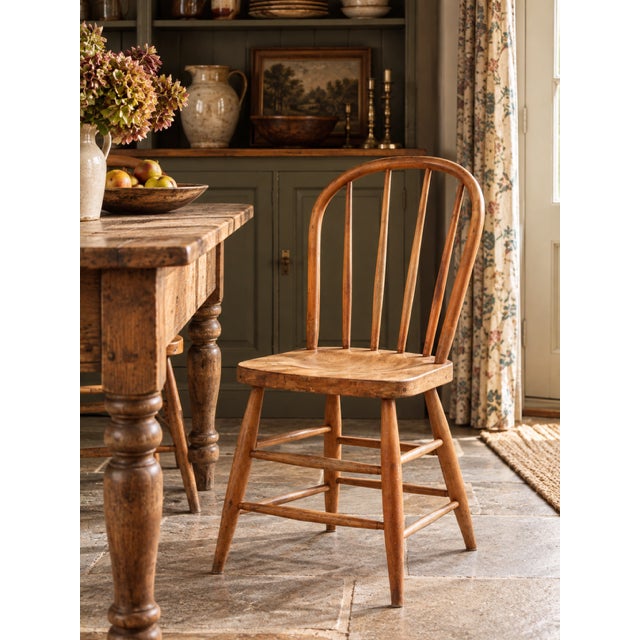 A vintage 1930s Windsor-style farmhouse chair featuring a gracefully curved bow back with five slender spindles, a shaped...