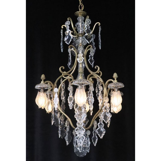 Louis XV style chandelier draped in clear pendeloque crystals, a brass scrolled frame, and an etched crystal ball shaped...