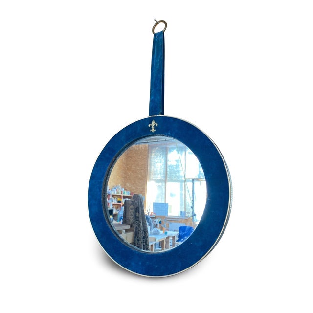 Circular wall mirror, framed with a metal band and topped with a decorative fleur-de-lis. It hangs from a matching bracket...