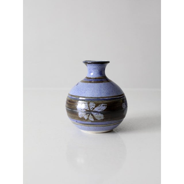 A vintage handmade studio pottery vase featuring a lavender blue glaze, earthy brown banding, and hand-decorated floral...