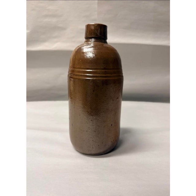 Elevate your space with this exceptional antique salt-glazed brown stoneware utility bottle, dating to the late 19th or...