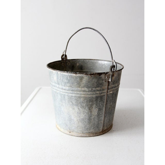 This vintage galvanized metal bucket features a classic utilitarian design with a curved handle for easy carrying....