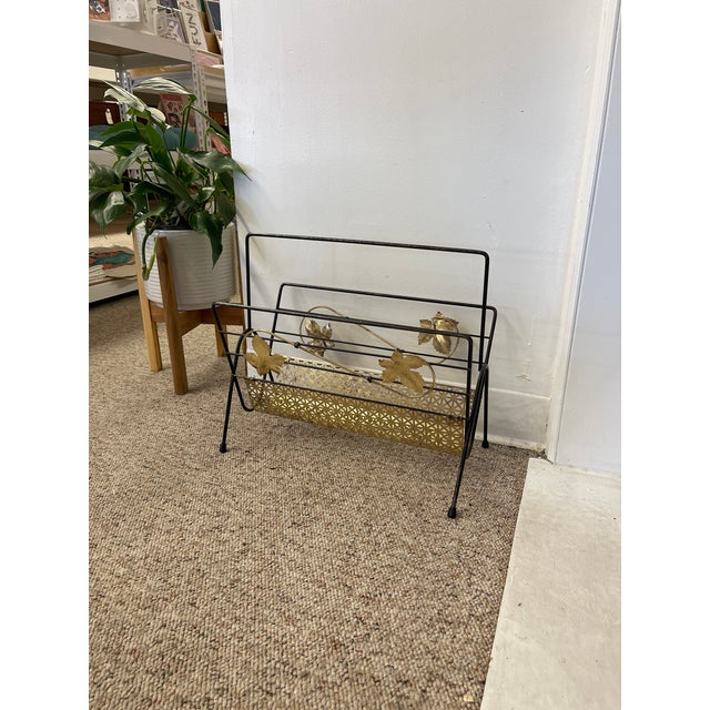 This vintage mid-century modern magazine rack features a striking combination of black wrought iron and decorative brass...