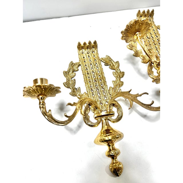 A decorative pair of vintage brass wall candle sconces in the Louis XVI style, featuring architectural laurel and acanthus...