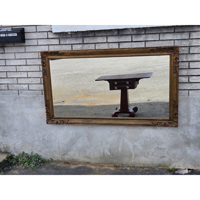 This mid-twentieth-century heavily carved wall fireplace mirror is an antique piece with a Victorian-era design. The...