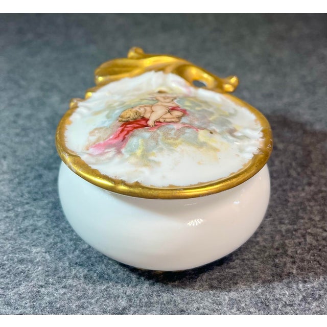 Hand painted fine antique porcelain pill/trinket box depicting a pair of cherubs highlighted in thick gold. Attributed to...