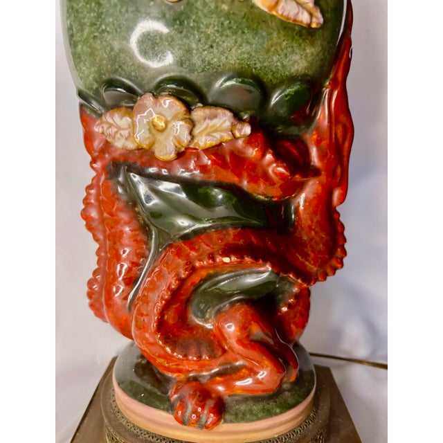 A wonderfully theatrical ceramic table lamp featuring a red-orange dragon curling around the lower body beneath a...