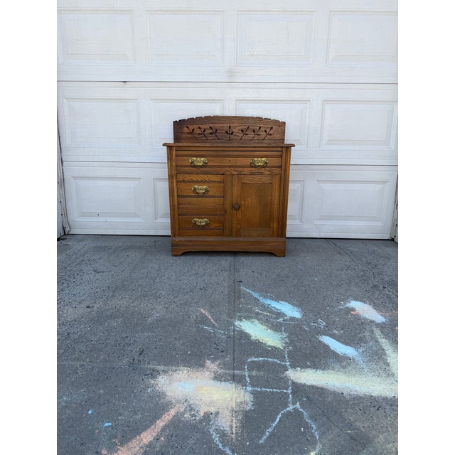 We have an antique oak washstand with a decorative carved backsplash, brass hardware, drawers, and cabinet storage for...