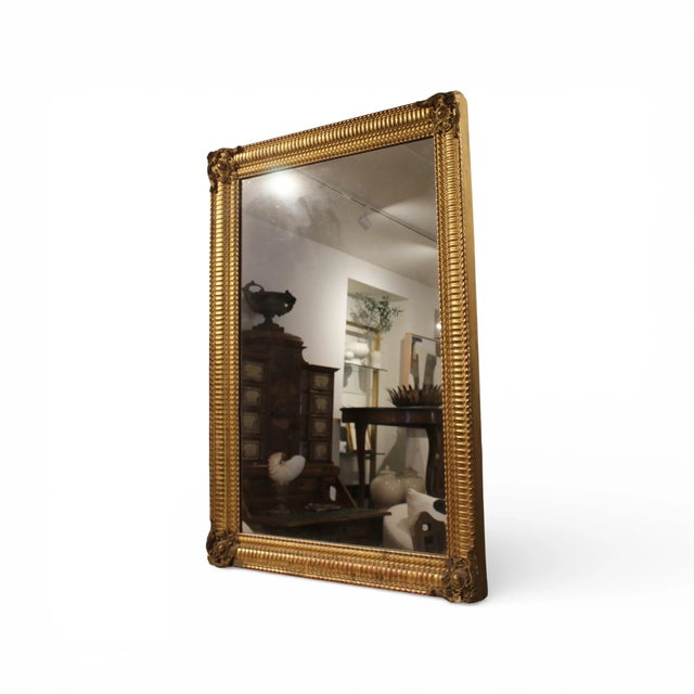 A 19th-century French Louis Philippe antique mirror featuring a gilded frame with elegant ripple detailing. The warm...