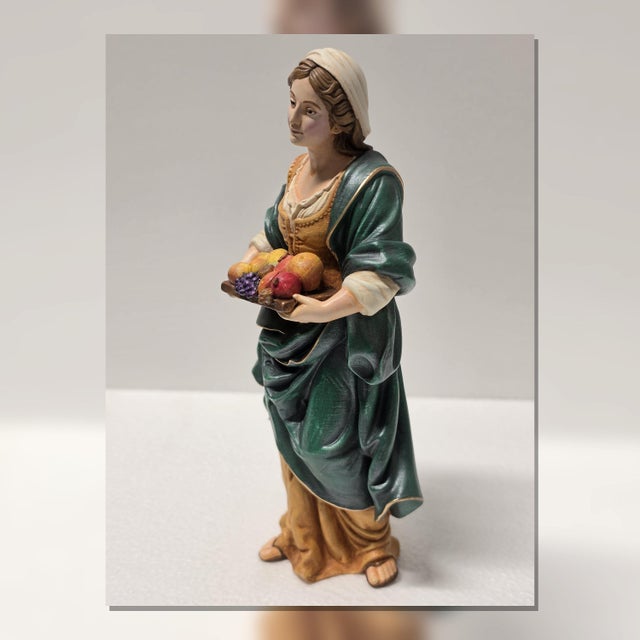 This figurine represents a standing village woman holding a tray of fruit at waist height, interpreted through classical...