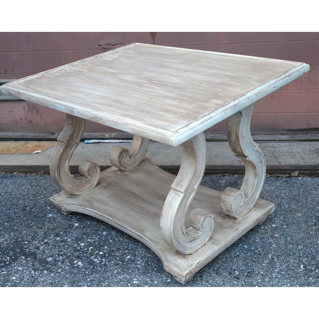 A Mid Century distressed white washed rectangular two tier side table with scroll details. Measures 28" in width, 24" in...
