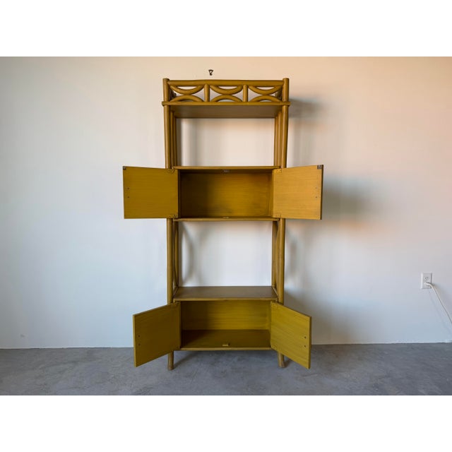 Charming vintage bent rattan bookcase featuring a warm mustard yellow finish with sculptural bamboo-style curves and...