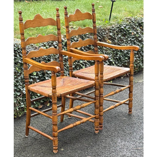 Charming pair of rustic country-style armchairs featuring beautifully shaped ladder backs, turned spindle posts, and...