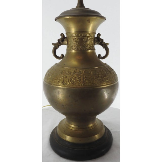 We are offering a cast brass lamp with elegantly scrolled arms and detailed embossing. The lamp sits atop a black base....