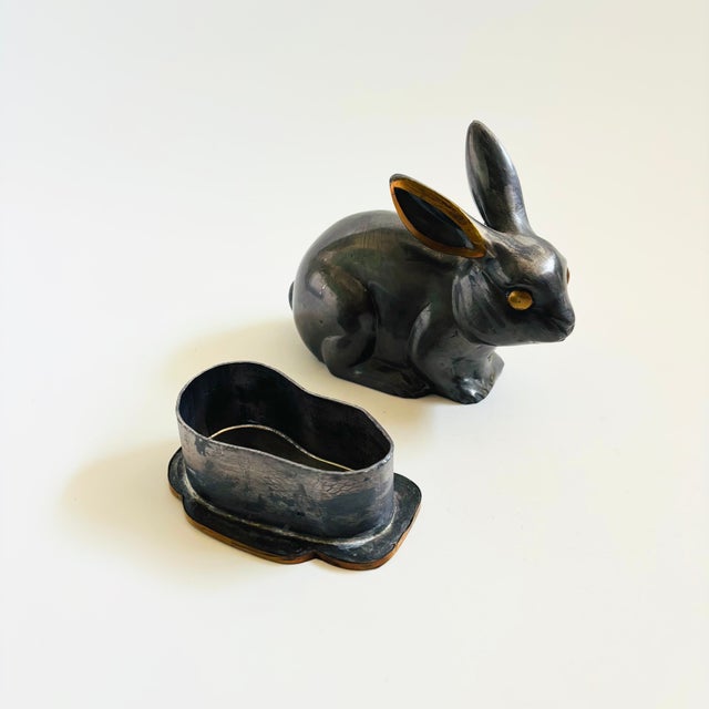 A vintage pewter rabbit shaped box. Dark silver color to the metal with brass accents. The top lifts off to reveal a small...