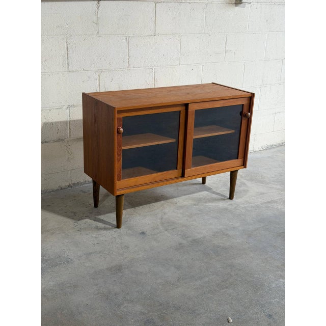 Pair of vintage Danish Mid Century Modern teak cabinets featuring sliding glass doors, adjustable shelving, and elegant...