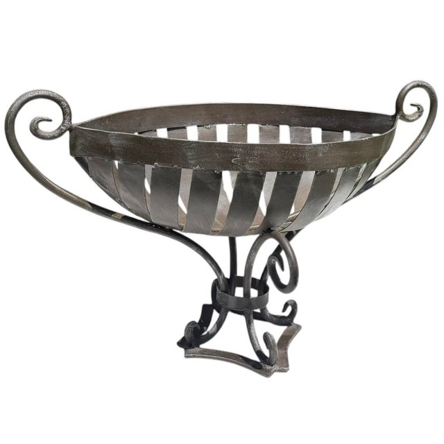 A substantial vintage wrought iron centerpiece bowl featuring an elongated basket-form design with elegant scroll handles...