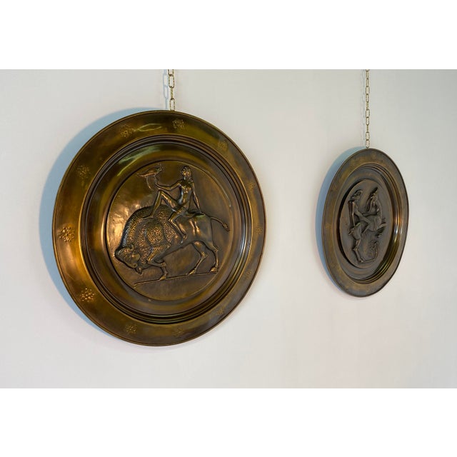 Pair of hanging brass plates produced in Italy in the 1940s. The classic art deco subjects are represented and are in...