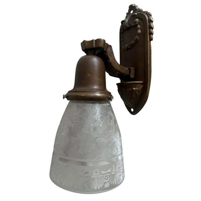 These antique wall sconce feature an ornate backplate with laurel wreaths and textured, bell-shaped frosted glass shades...